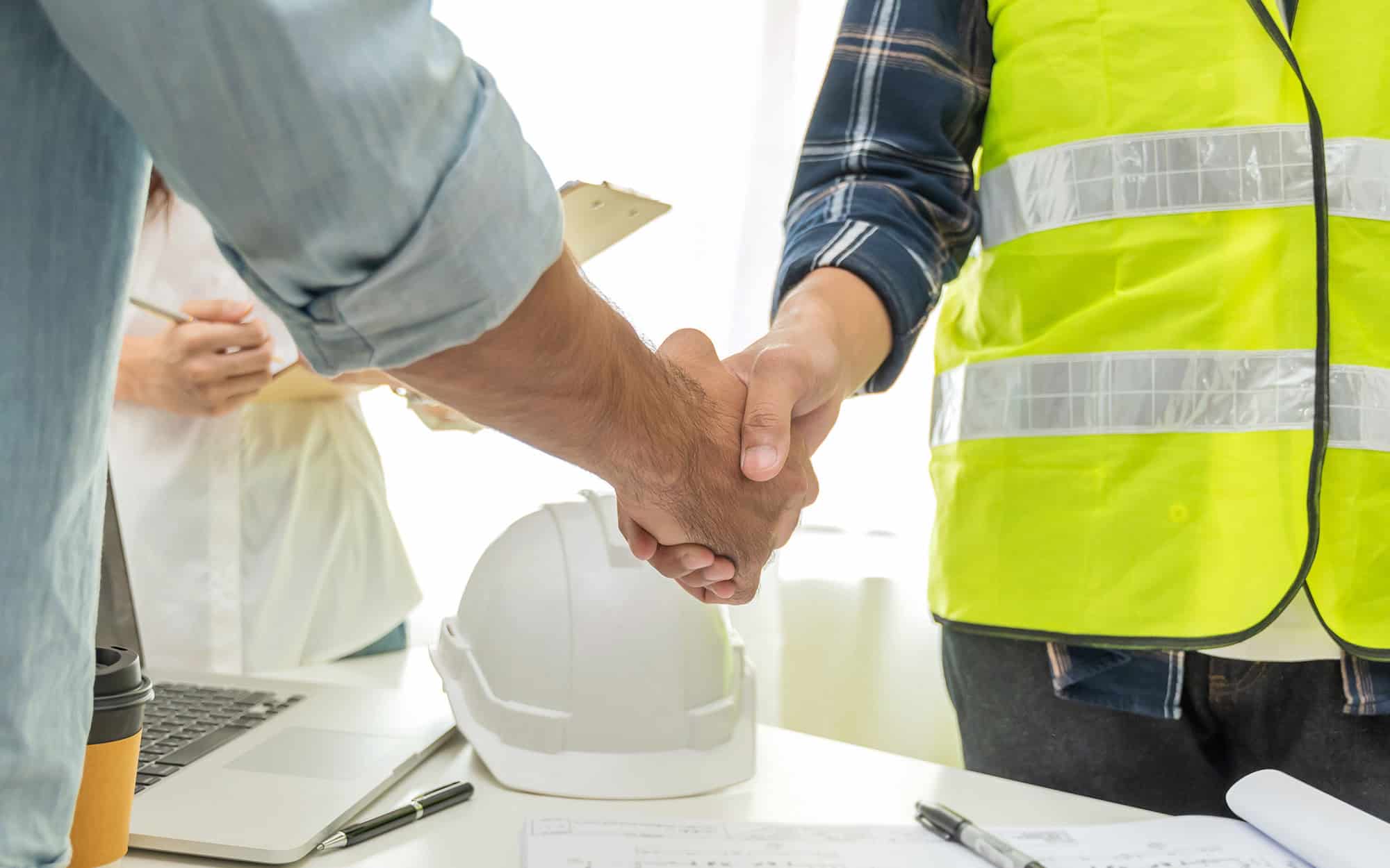 Side view of two construction workers shaking hands in clean office